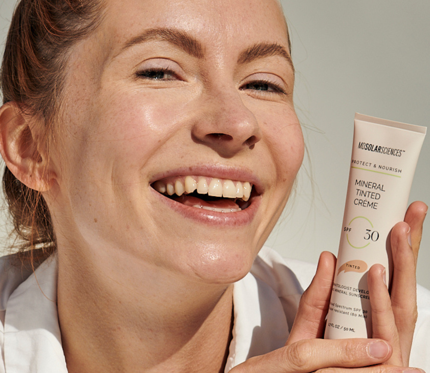 Woman holding a tube of 'Mineral Tinted Creme' sunscreen